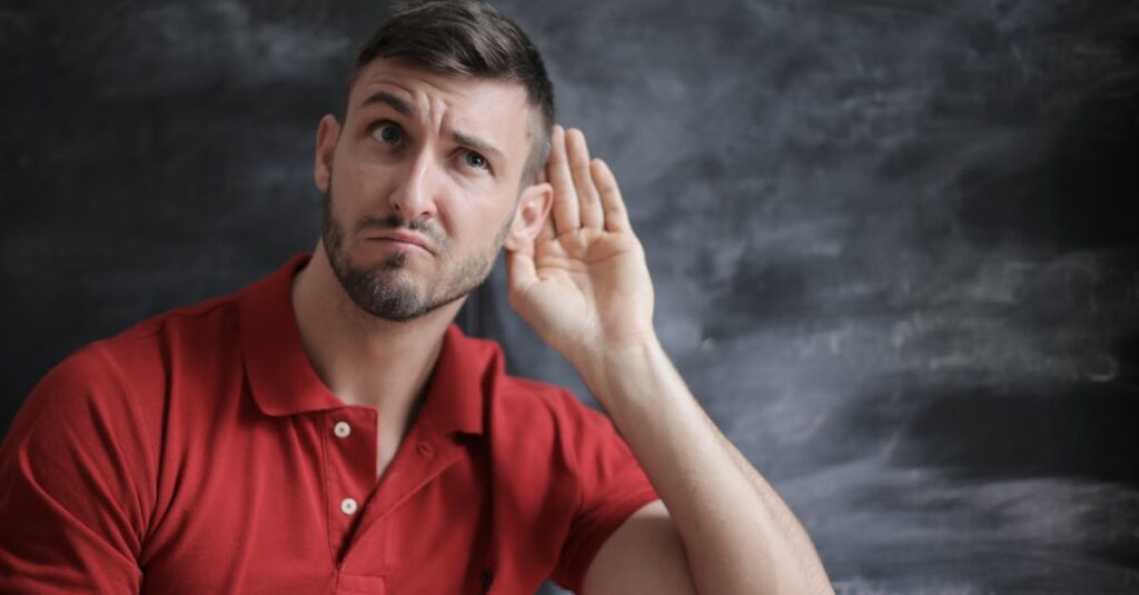 Thoughtful man listening intently against a chalkboard background in a red polo shirt.